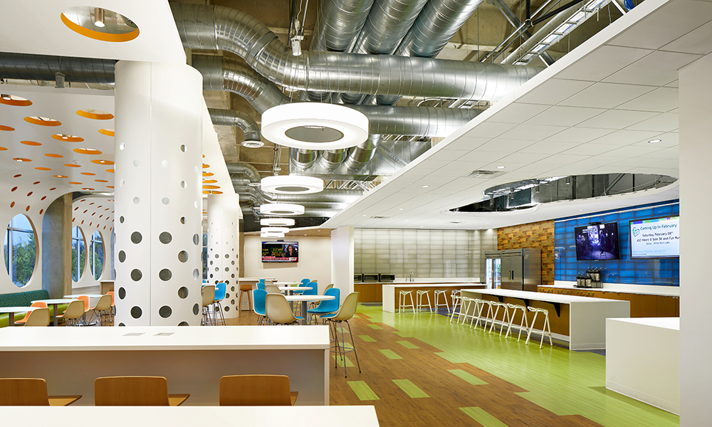 <p>The technology-ready Café is a place for employees to eat, work alone or in groups, collaborate, or hold meetings for up to 250 people. Located along an exterior wall, the Café contributes to employee well-being, affording daylight and views to the outside framed by custom designed window port holes. The industrial feel of the building was retained in the exposed concrete and refined elements of the suspended perforated ceiling feature, which serves to lower the volume of the large space and create a more intimate feel. </p>
