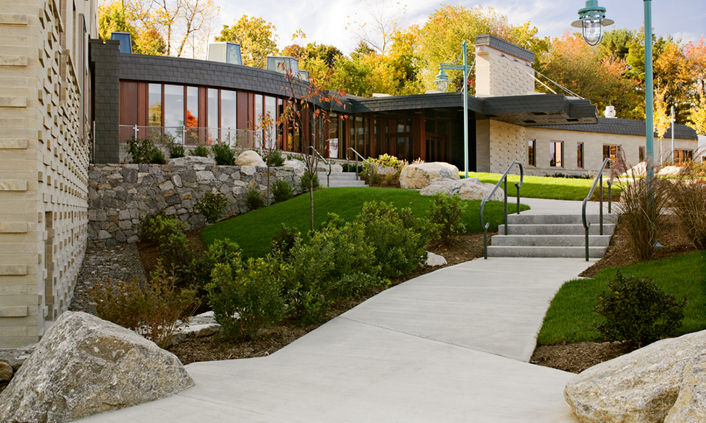 <p>The landscape is conceived as a stream/river flowing through the site, a nod to the origins of the community, originally dependent upon its rivers for economic success. The “river” starts at the top of the ridge, flows into the courtyard, travels into the lobby and continues on to form the entry walkway that connects the main vehicular access with the front door in the form of a meandering “stream”, replete with stone boulder edging salvaged from the site.</p>
