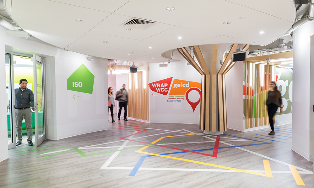 <p>The second-floor entry lobby, with its signature “tree,” provides informational wayfinding through a complementary color-coded flooring design and wall signage for Global Education and Career Development (GECD), the International Students Office (ISO), the International Scholars Office (ISchO), the Writing, Rhetoric, and Professional Communications program (WRAP), and the Writing and Communication Center (WCC) visitors.</p>
