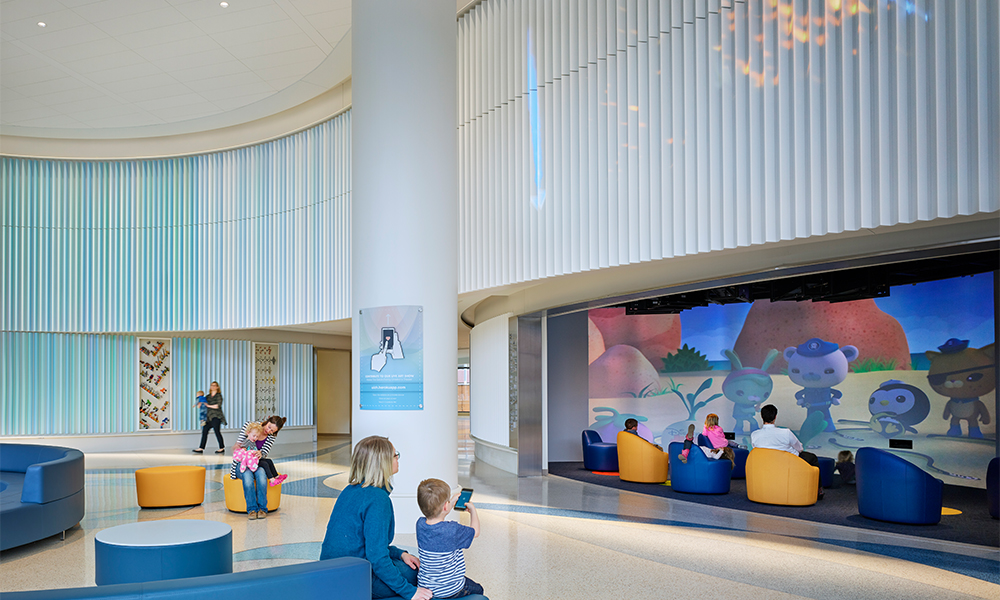 <p>In the lobby, children and families are invited to use technology to create images that project on the white triangle wall through an app on their phone or iPad.</p>
